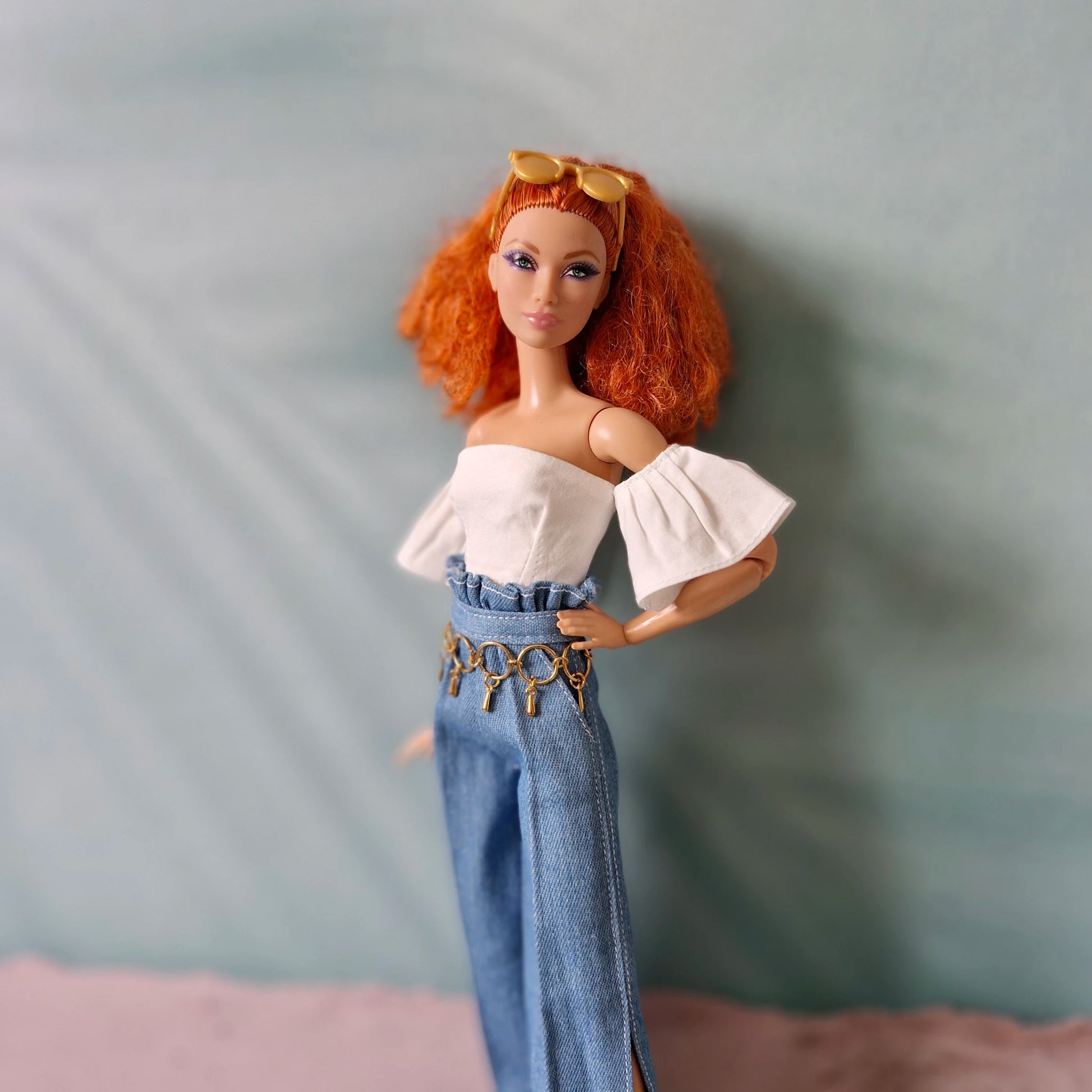 Doll with red hair wearing a white top and blue jeans against a gray background