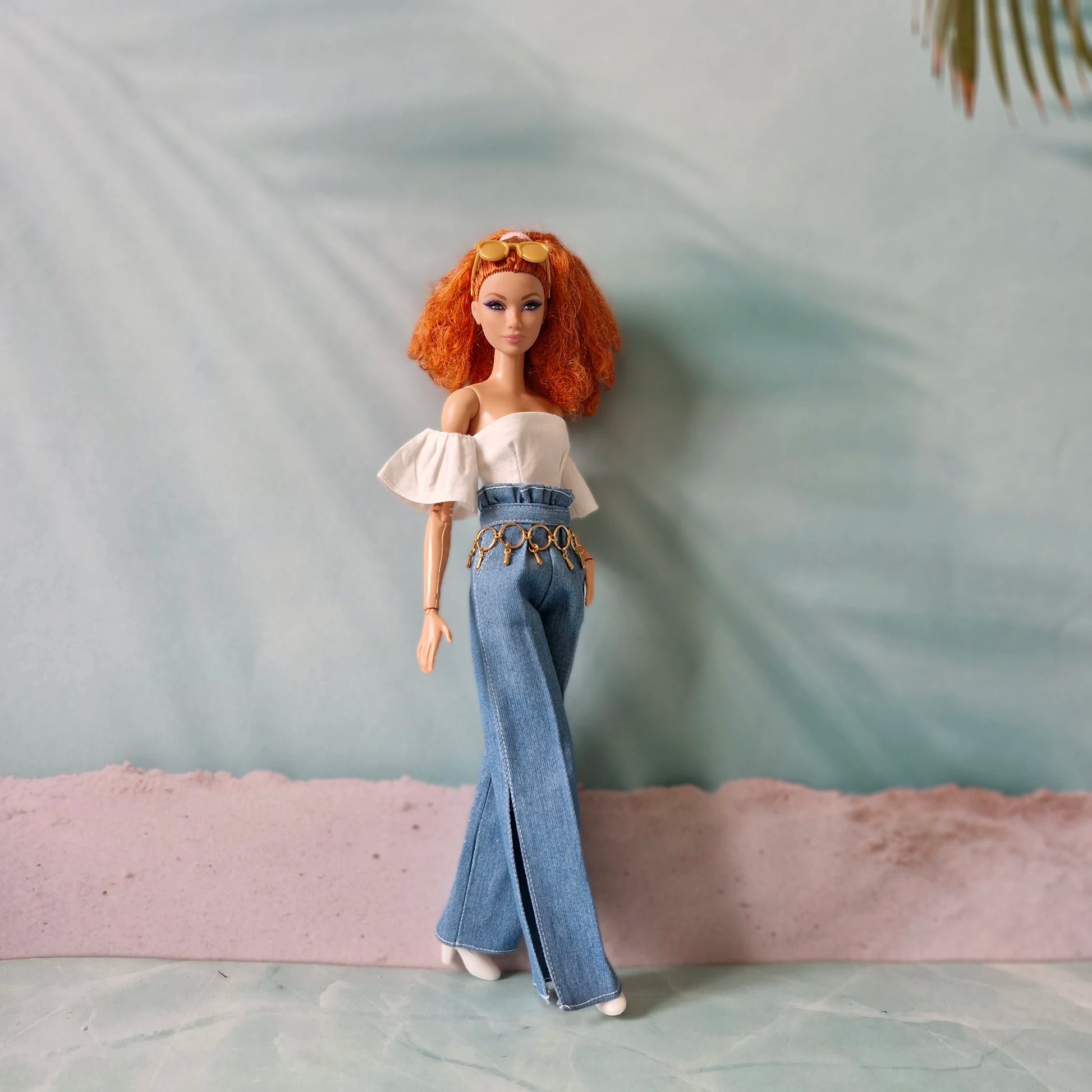 Barbie doll with red hair wearing a white top and blue jeans on a textured surface.