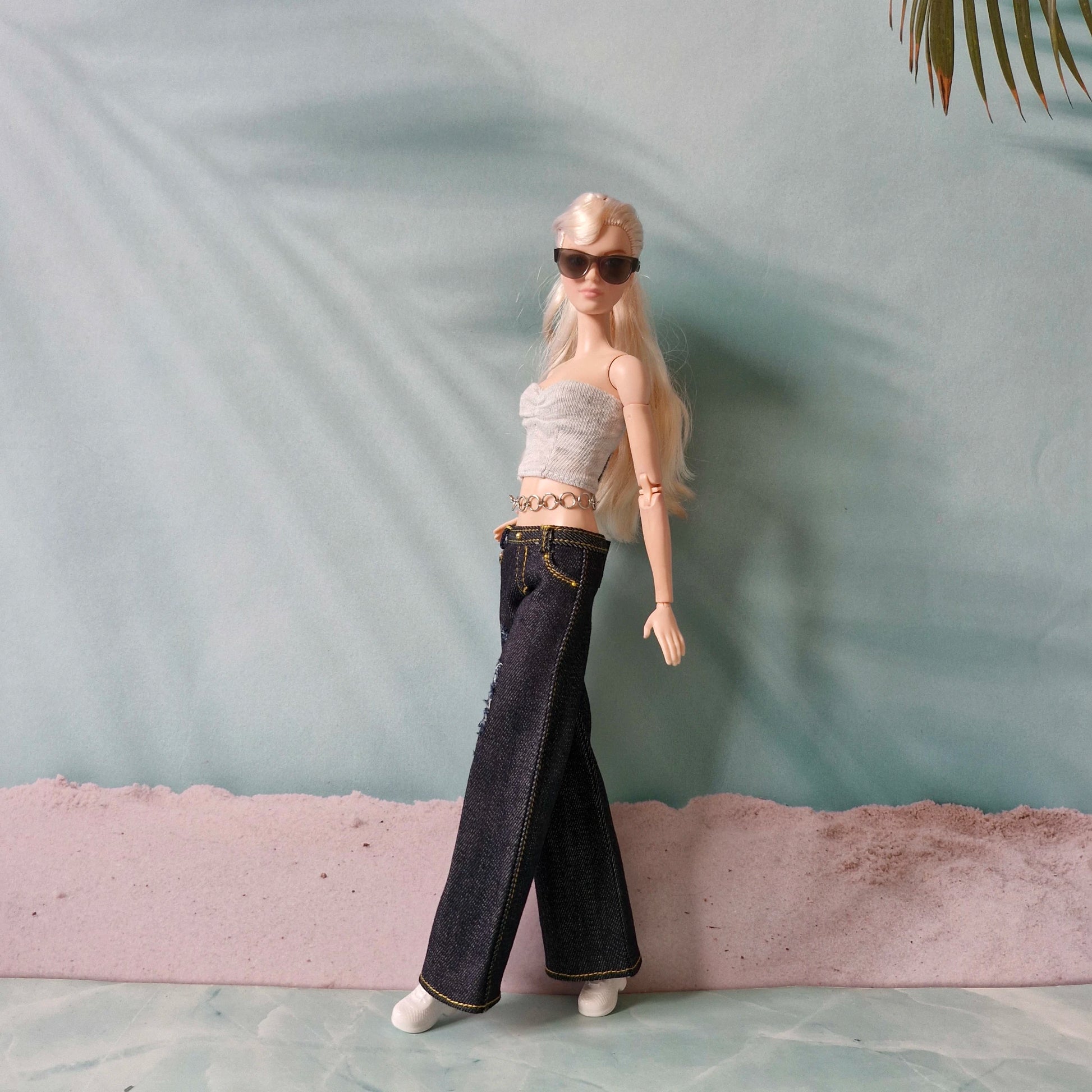 Barbie doll wearing a crop top and jeans with sunglasses against a light blue background