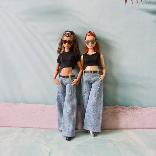 Two dolls wearing black tops and gray pants against a plain background