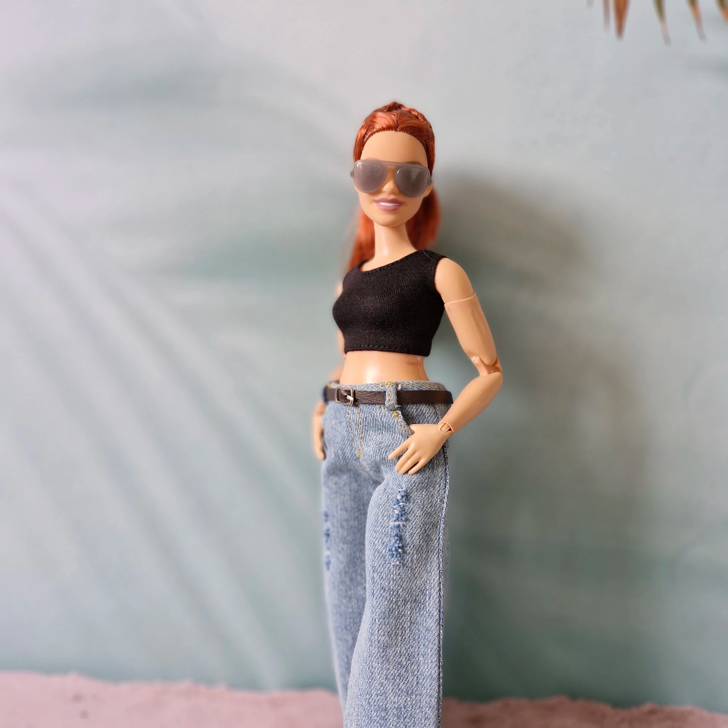 Barbie doll with red hair, black top, and blue jeans against a neutral background