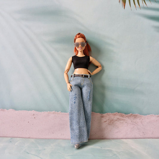 Doll with red hair, black top, and blue jeans standing against a light green wall.