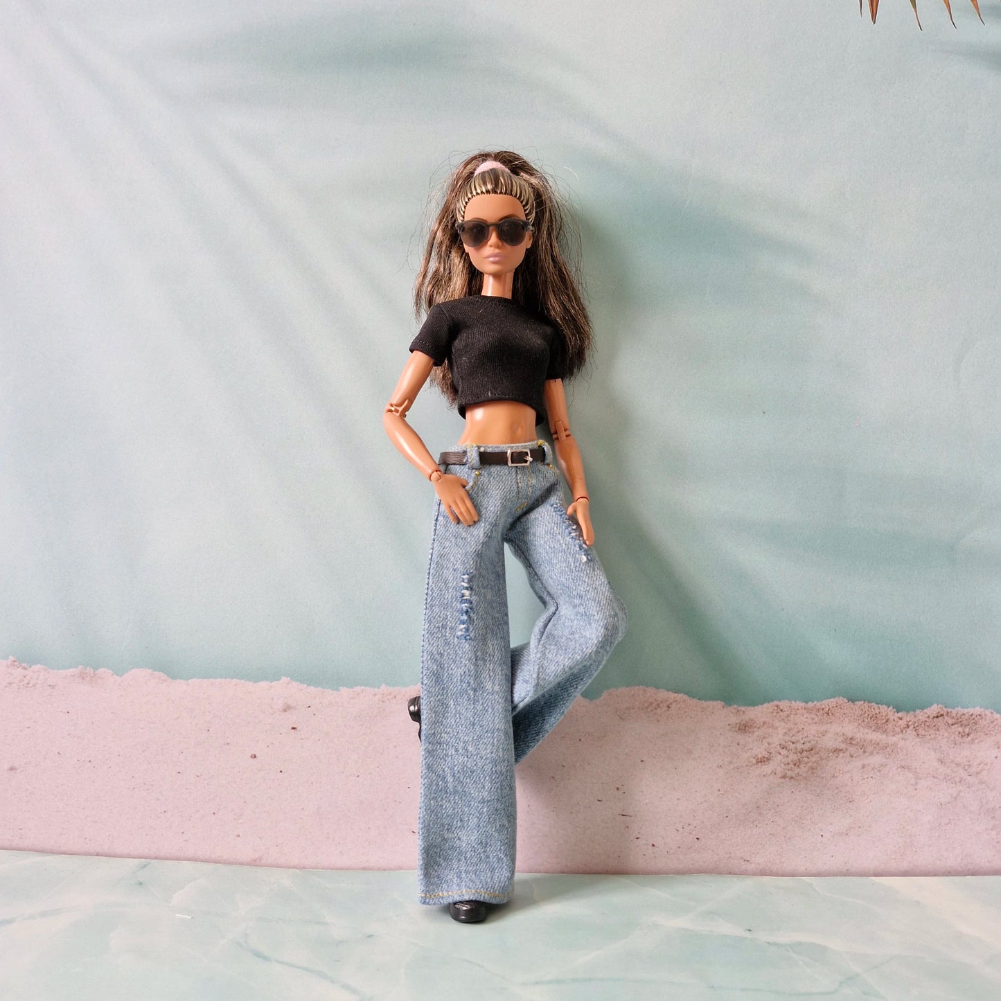 Barbie doll wearing a black top and gray jeans with sunglasses on a light green background