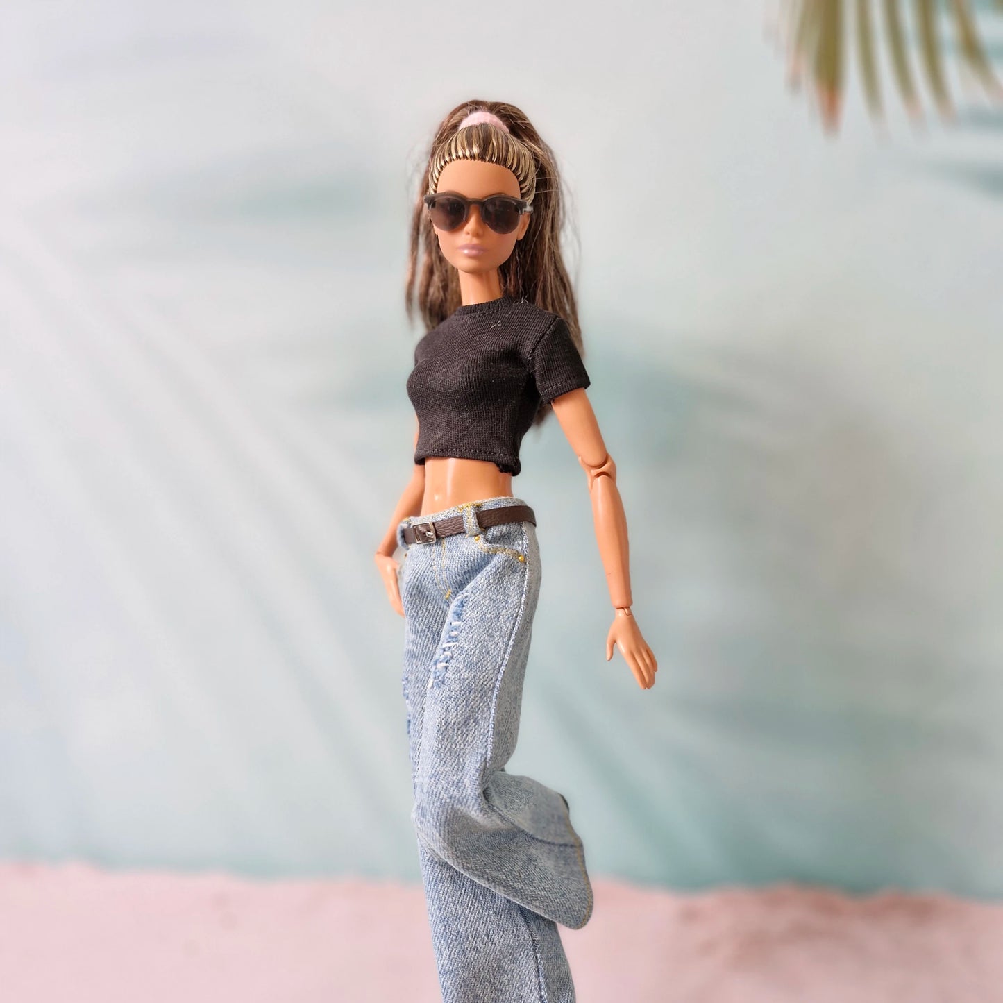 Barbie doll wearing sunglasses, a black top, and blue jeans against a light background