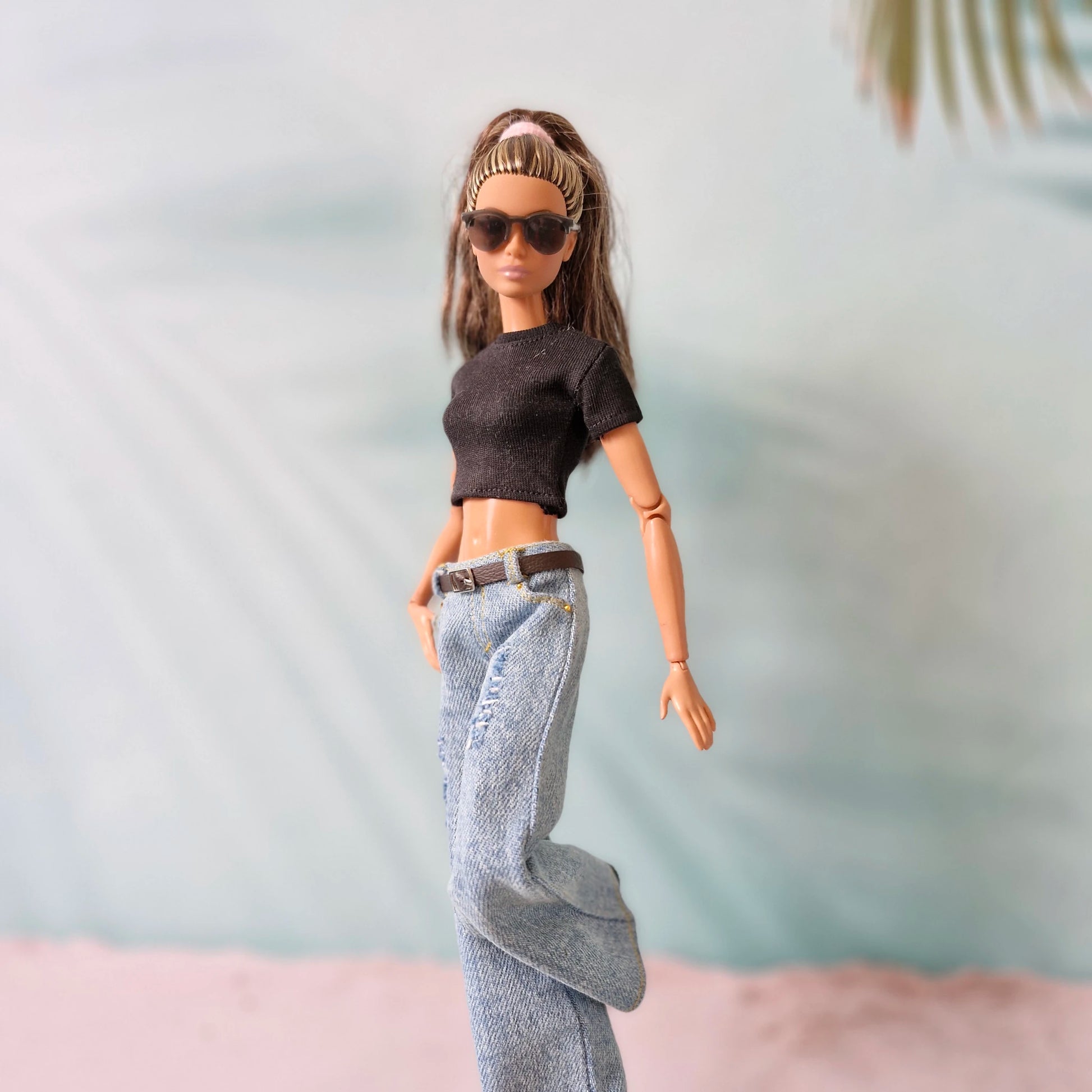 Barbie doll wearing sunglasses, a black top, and blue jeans against a light background
