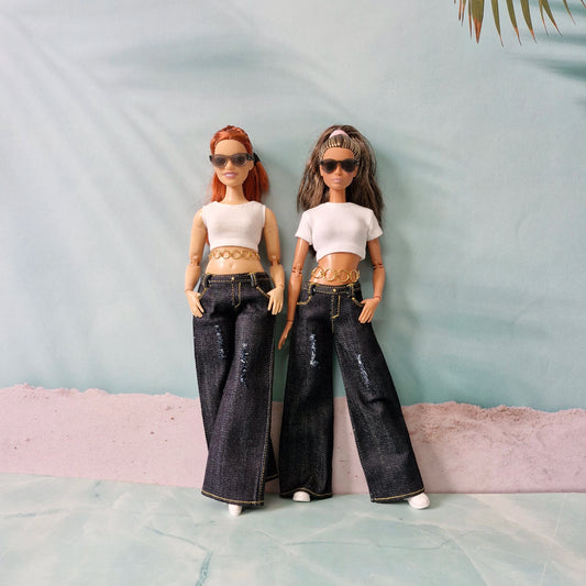 Two dolls wearing matching outfits with white tops and dark jeans against a light blue background.