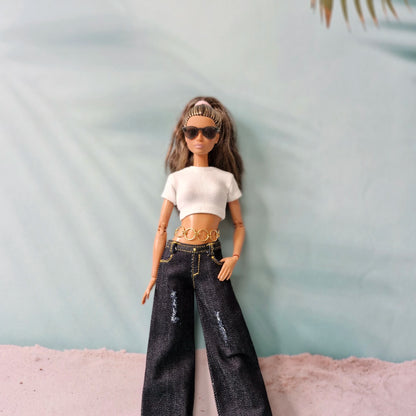 Barbie doll wearing a white top, black jeans, and sunglasses against a light blue background.