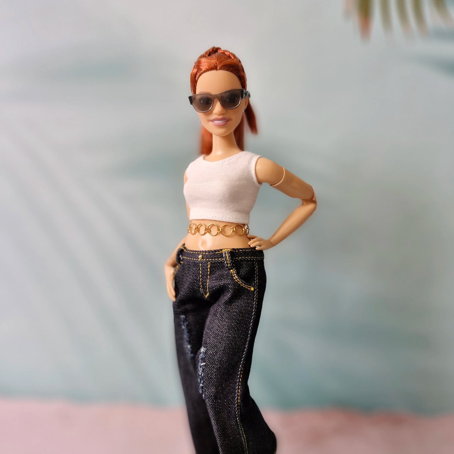 Barbie doll wearing sunglasses, a white top, and black jeans with a blurred background