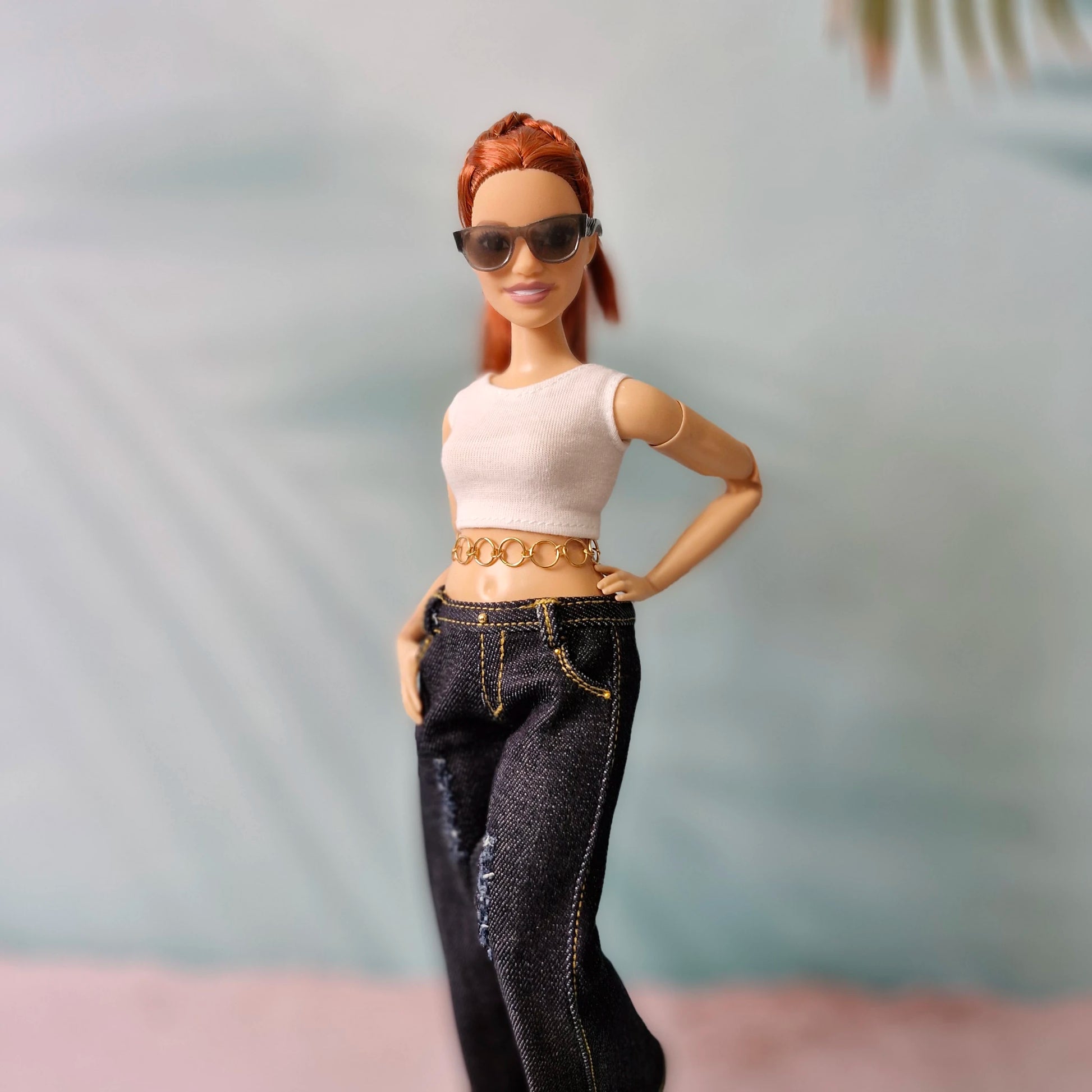 Barbie doll wearing sunglasses, a white top, and black jeans with a blurred background