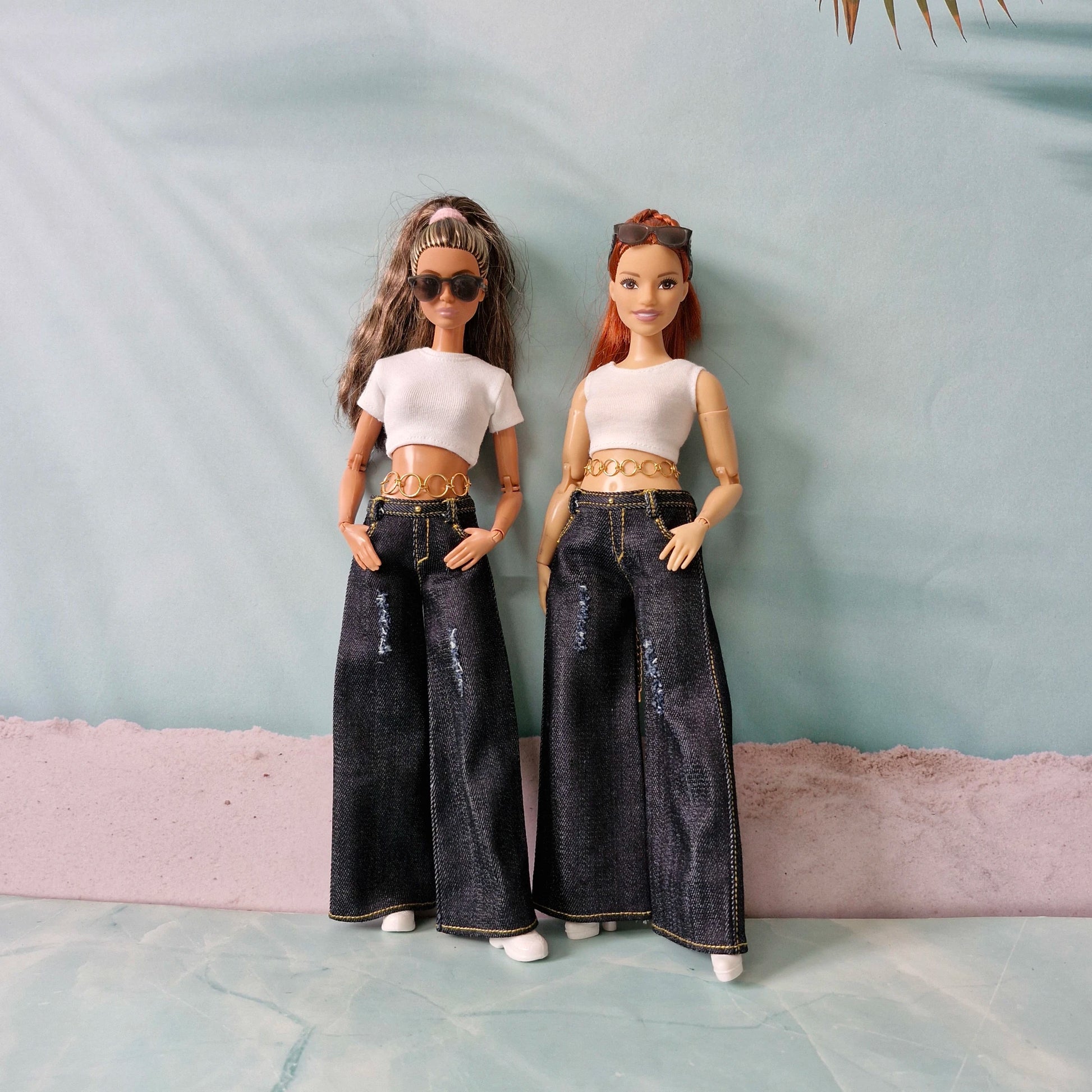 Two dolls wearing white tops and dark jeans against a light blue background