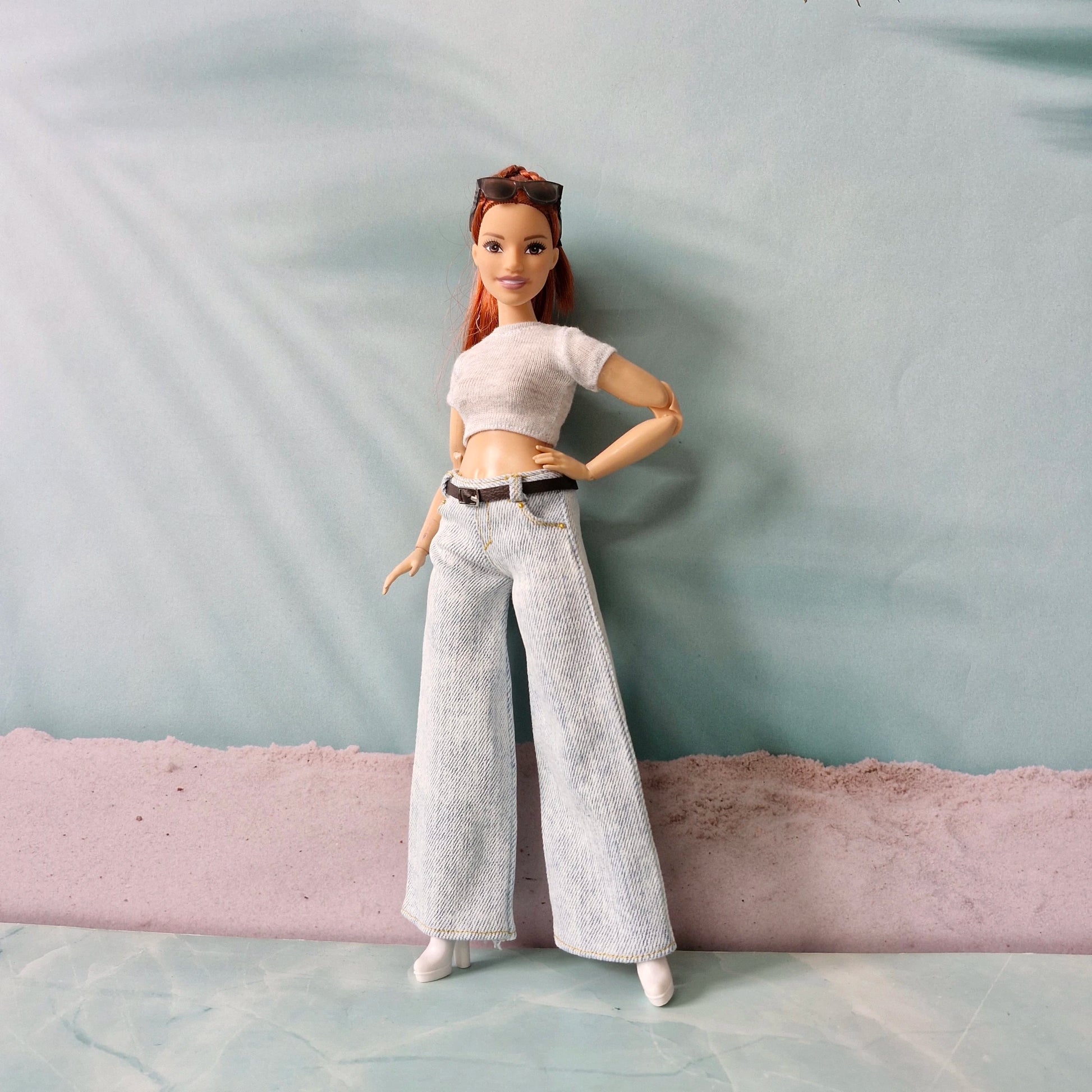 Barbie doll wearing a white crop top and light gray pants against a plain background