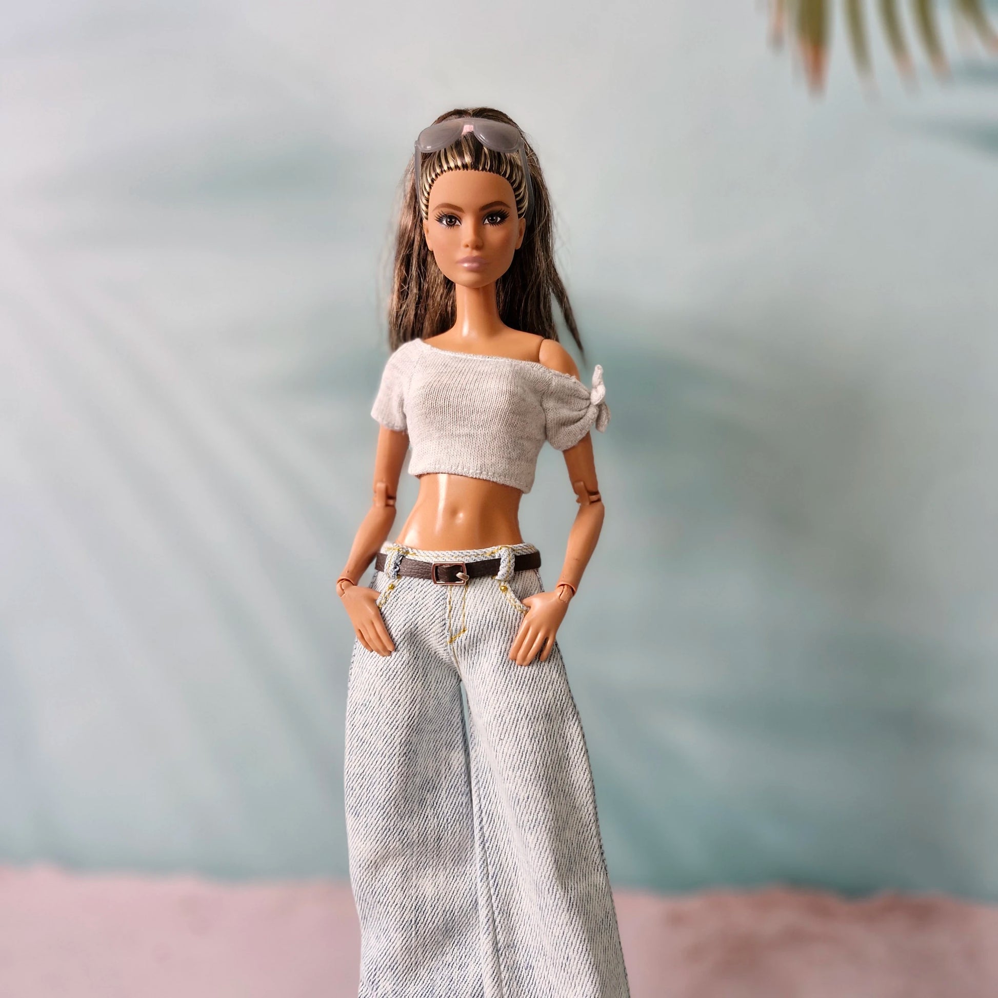 Barbie doll wearing a white top and patterned pants with a blurred natural background