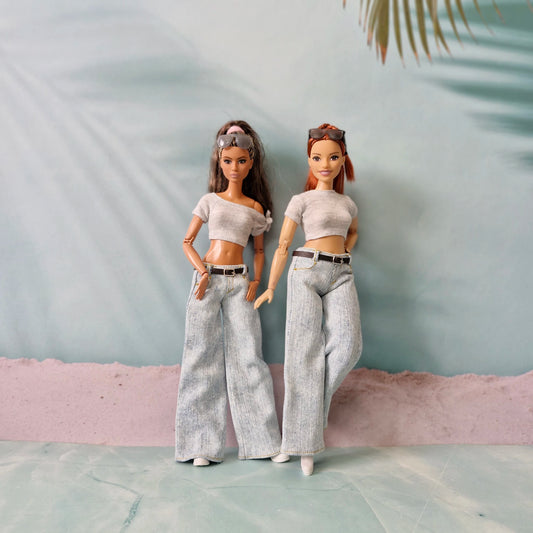 Two dolls wearing matching outfits with a neutral background