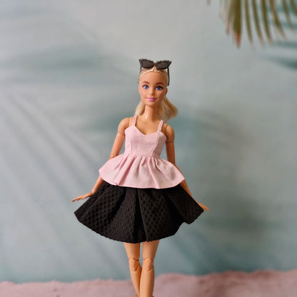 Barbie doll wearing a pink top and black skirt with a blurred background