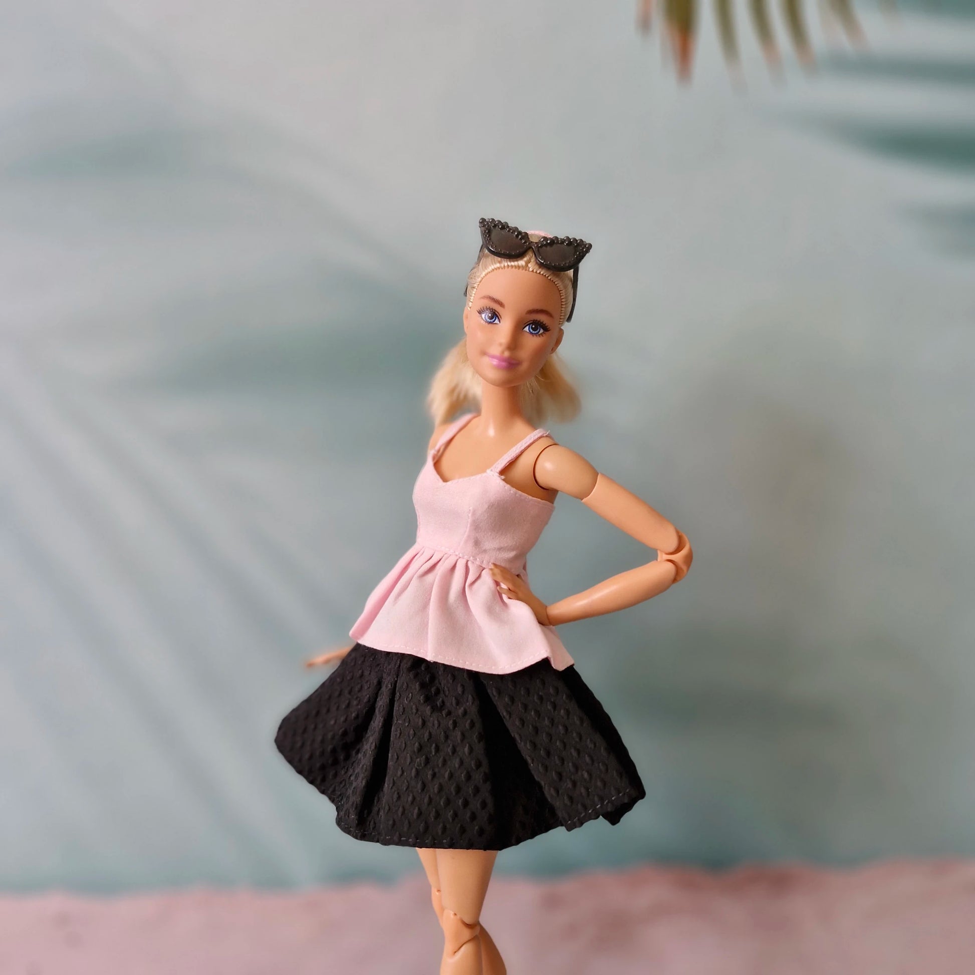 Barbie doll wearing a pink top and black skirt with sunglasses on head against a blurred background