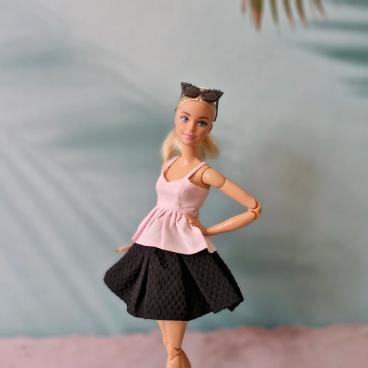 Barbie doll wearing a pink top and black skirt with sunglasses on head against a blurred background