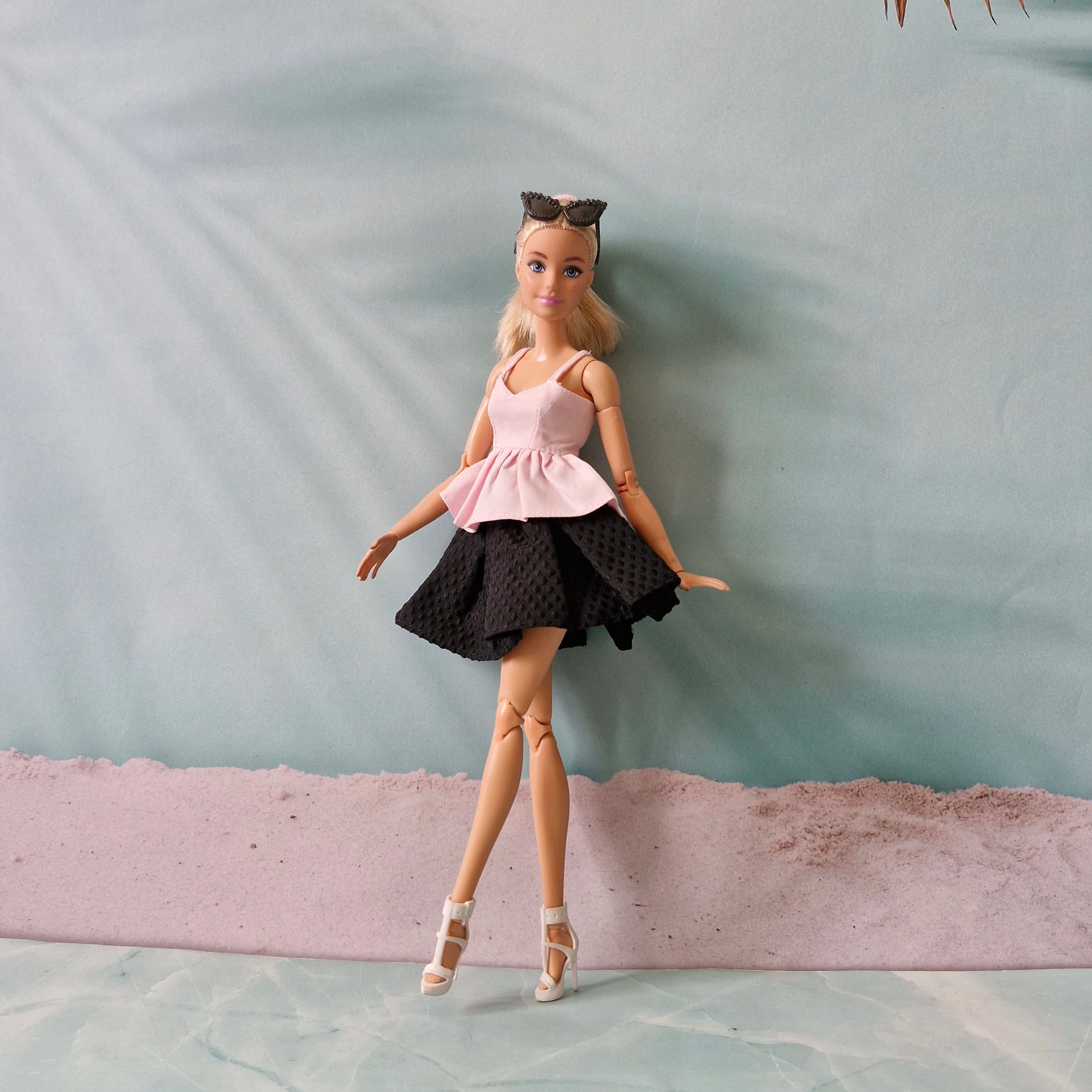 Barbie doll in a pink top and black skirt standing on a textured surface with a light blue background.