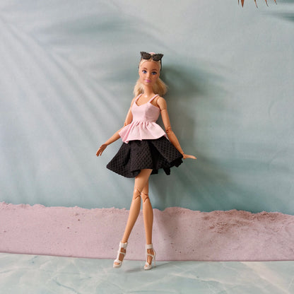 Barbie doll in a pink top and black skirt standing on a textured surface with a light blue background.