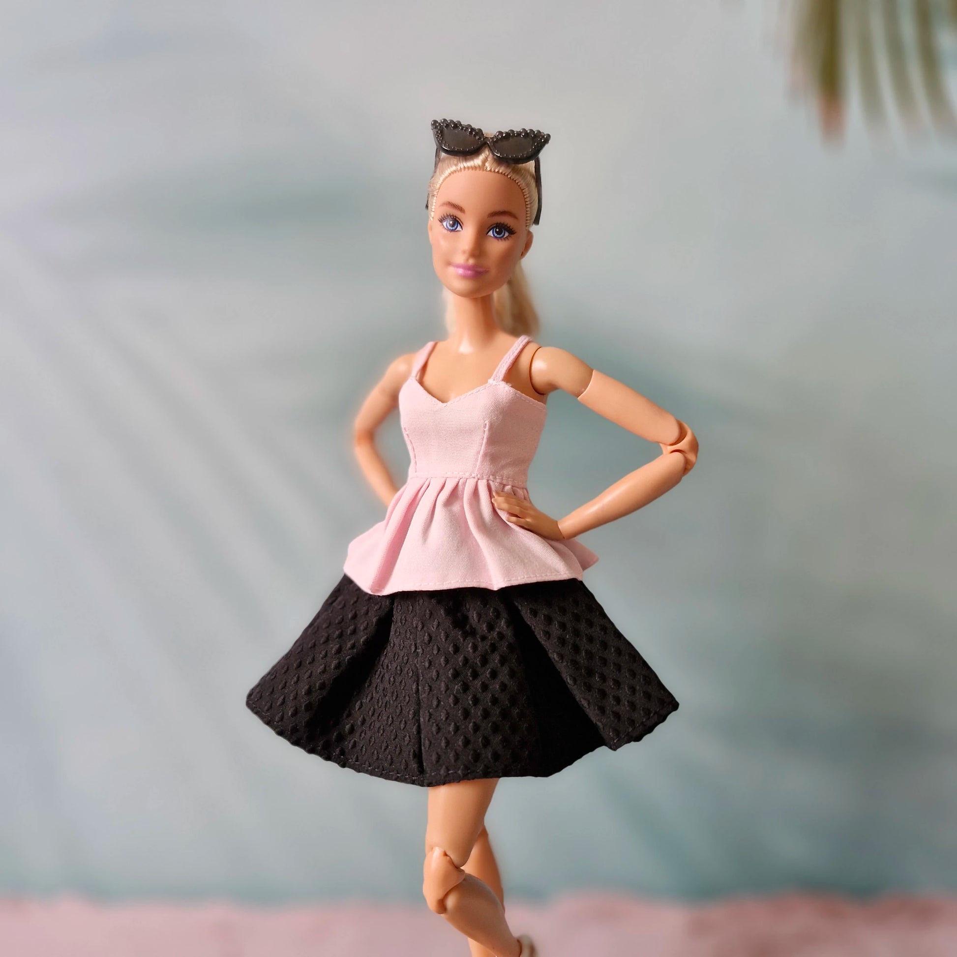 Barbie doll wearing a pink top and black skirt with a blurred background