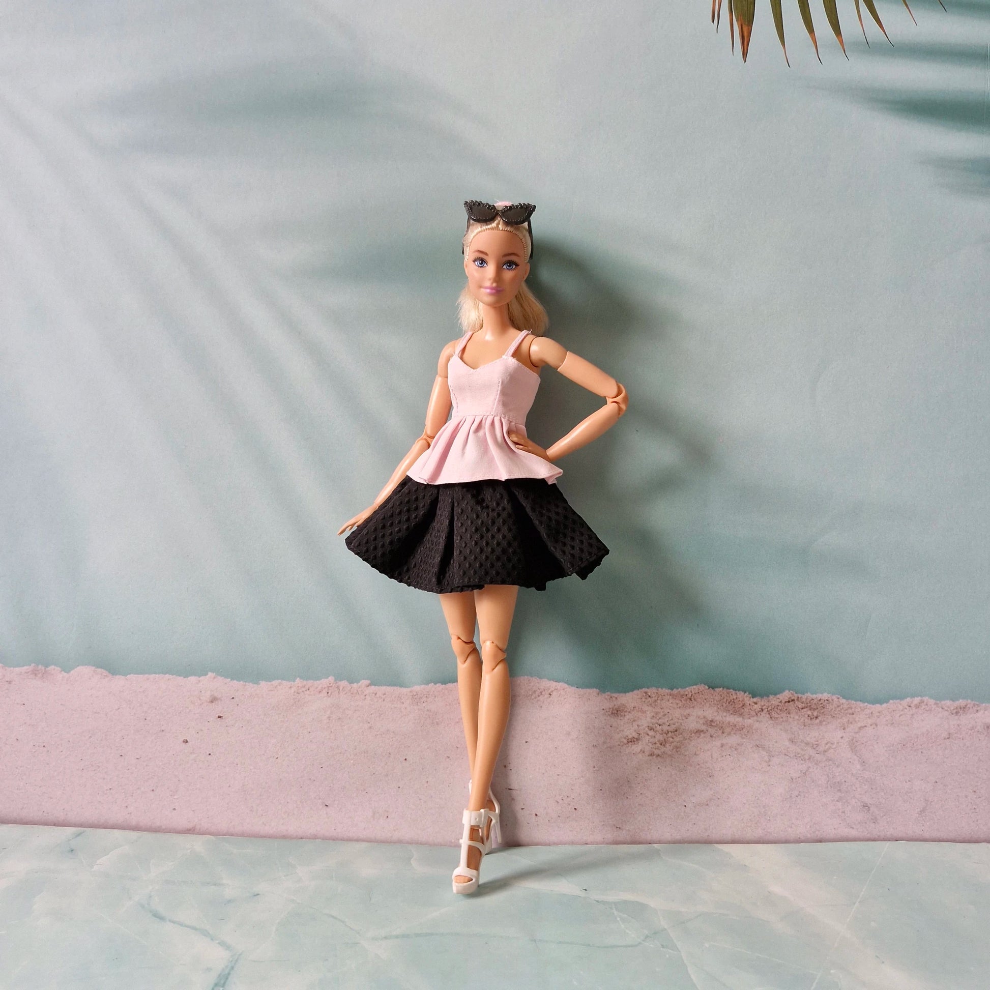 Barbie doll in a pink top and black skirt standing against a light blue wall.