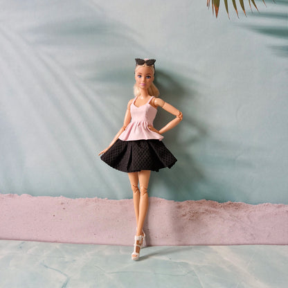 Barbie doll in a pink top and black skirt standing against a light blue wall.