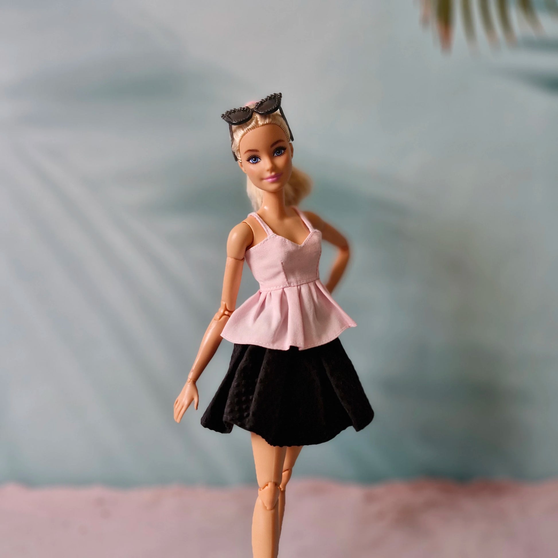 Barbie doll wearing a pink top and black skirt with a blurred background
