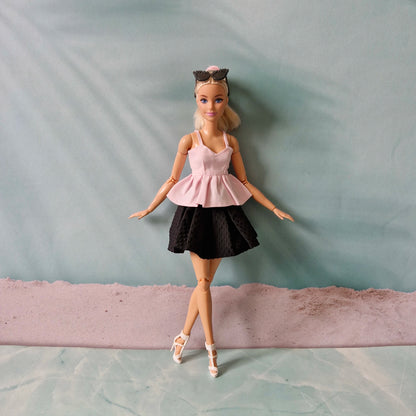 Barbie doll wearing a pink top and black skirt on a plain background
