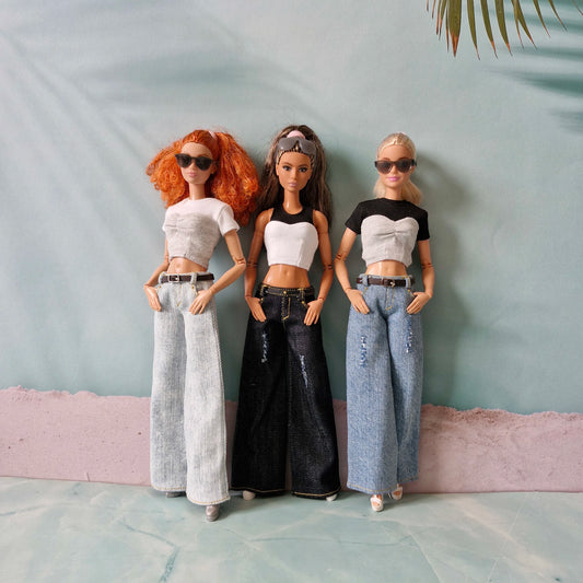 Three dolls in stylish outfits against a light blue wall.