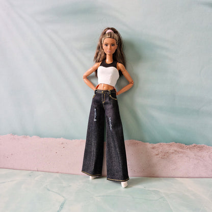 Barbie doll wearing a white top and black jeans standing on a textured surface with a light blue background.