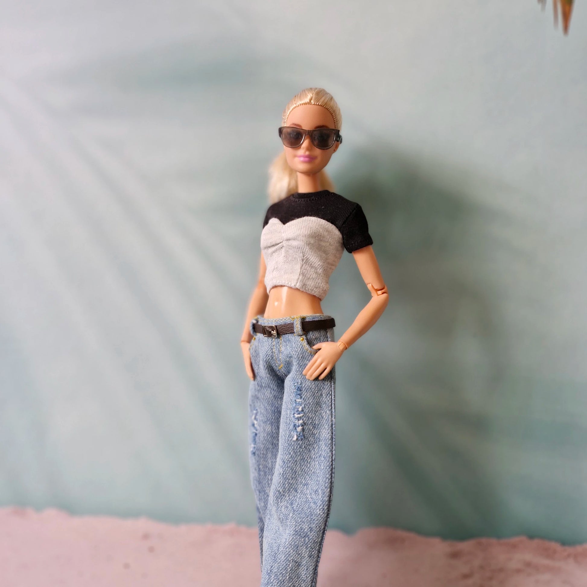 Barbie doll wearing a black and white top, gray pants, and sunglasses on a neutral background