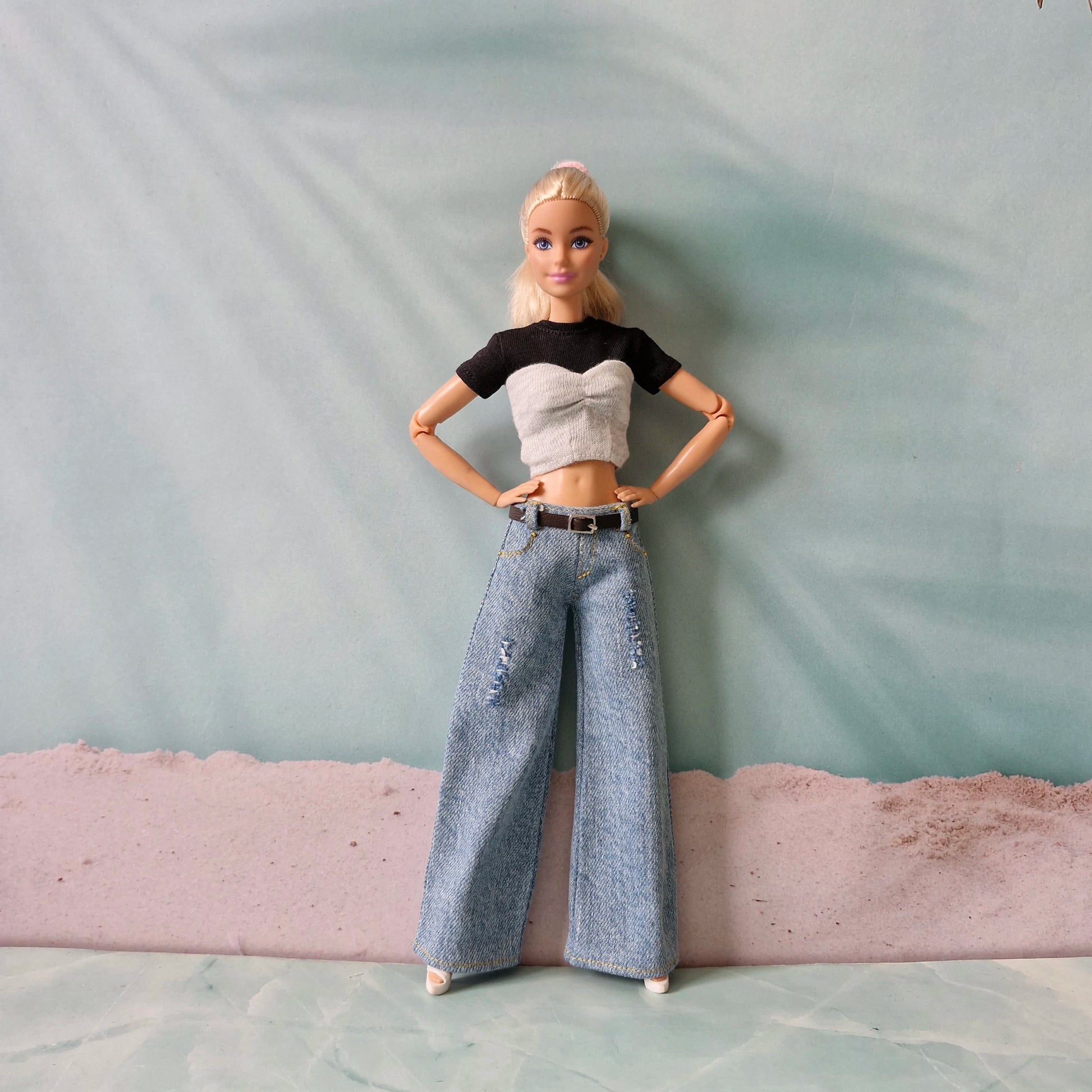 Barbie doll wearing a black crop top, gray sweater, and blue jeans against a plain background