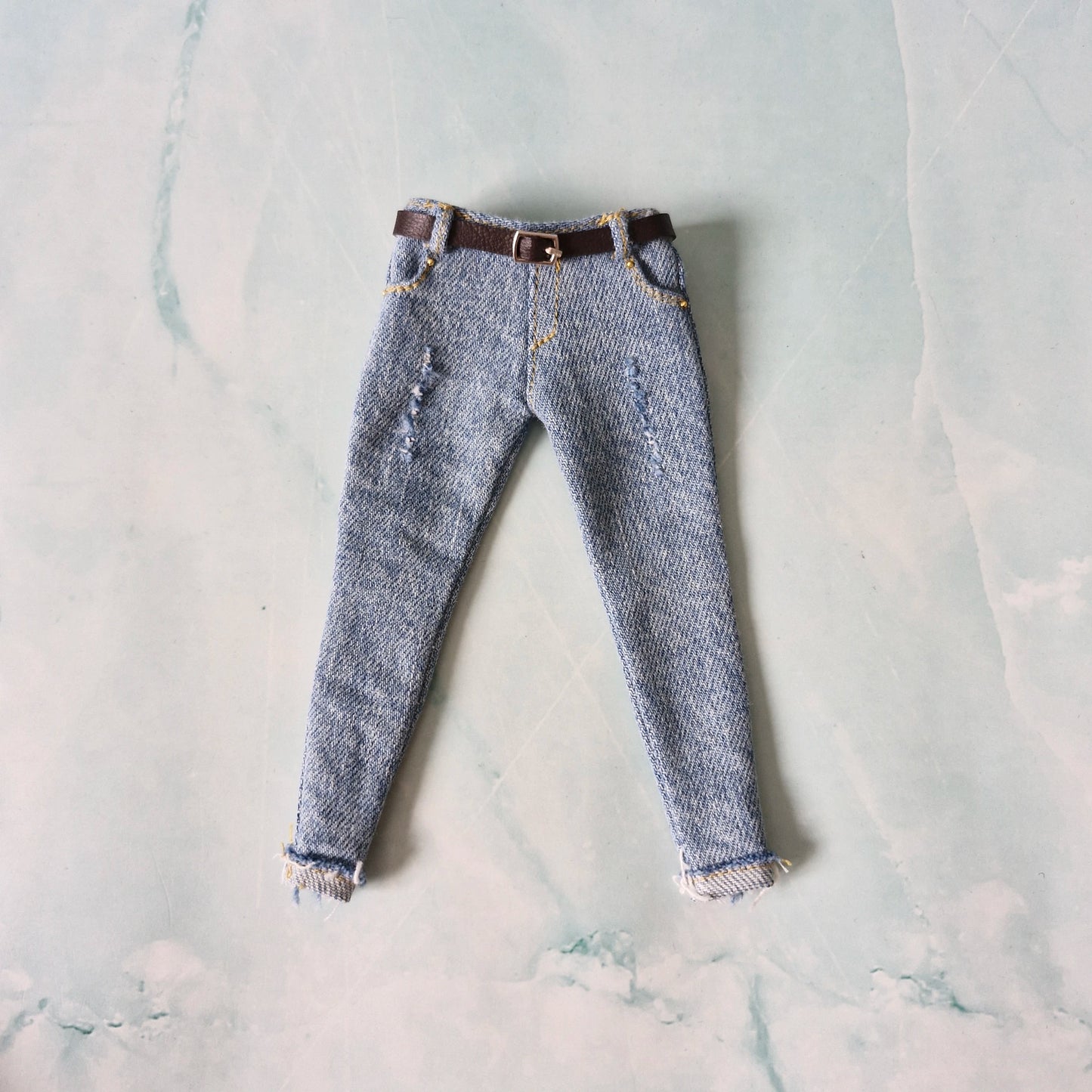 Pair of blue jeans with a brown belt on a light gray marble surface