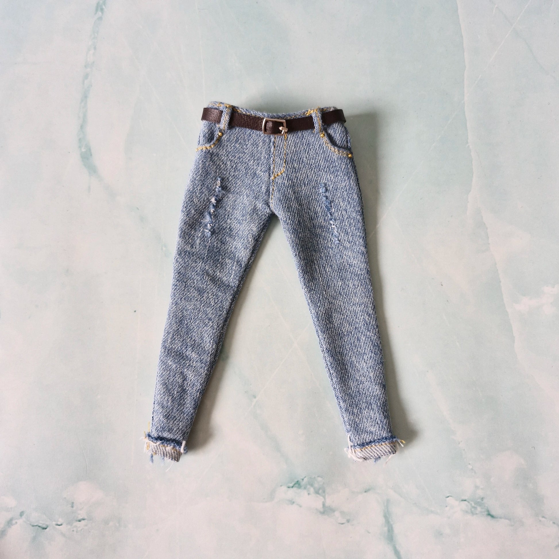 Pair of blue jeans with a brown belt on a light gray marble surface