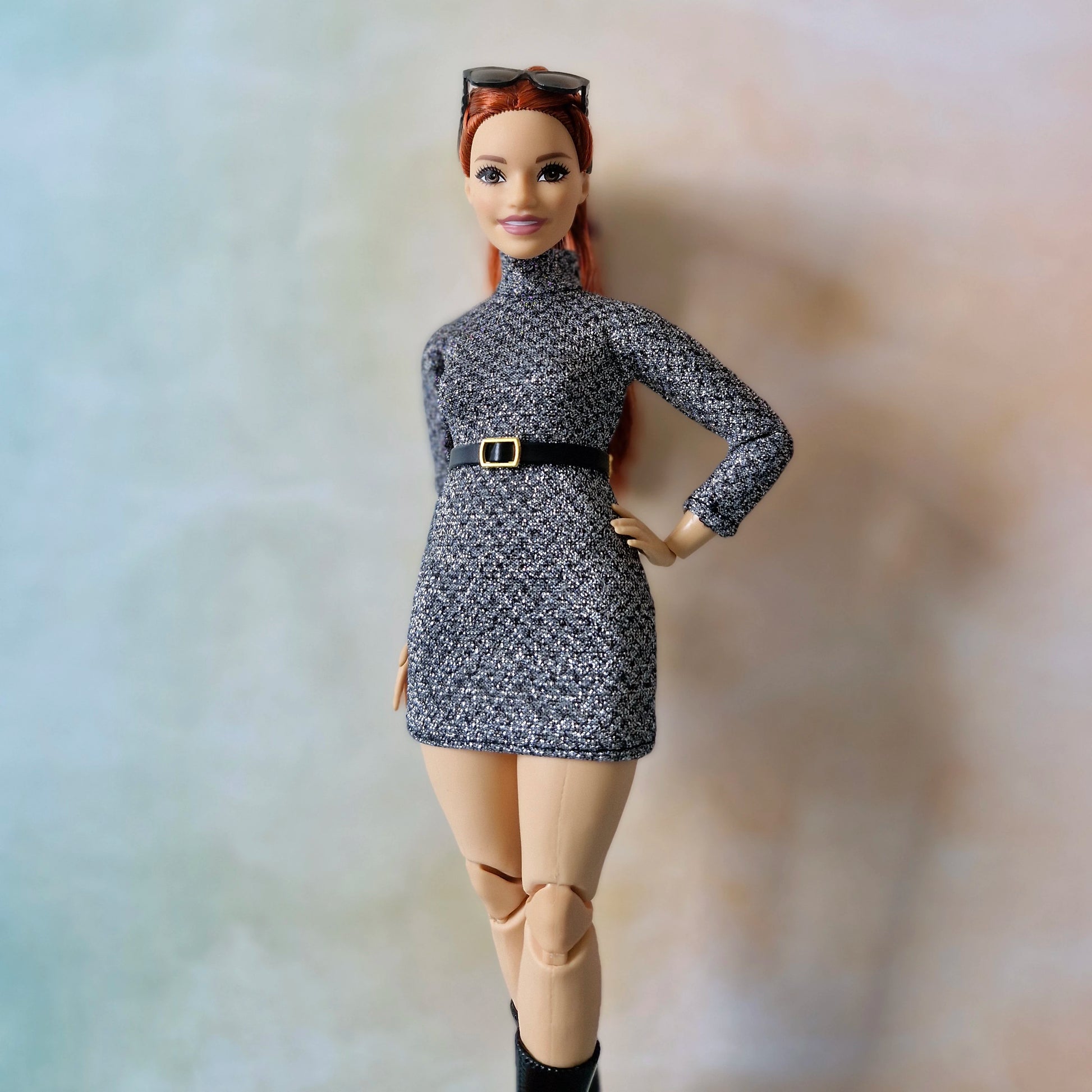 Barbie doll wearing a gray dress with a belt and beige pants against a neutral background
