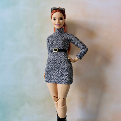 Barbie doll wearing a gray dress with a belt and beige pants against a neutral background
