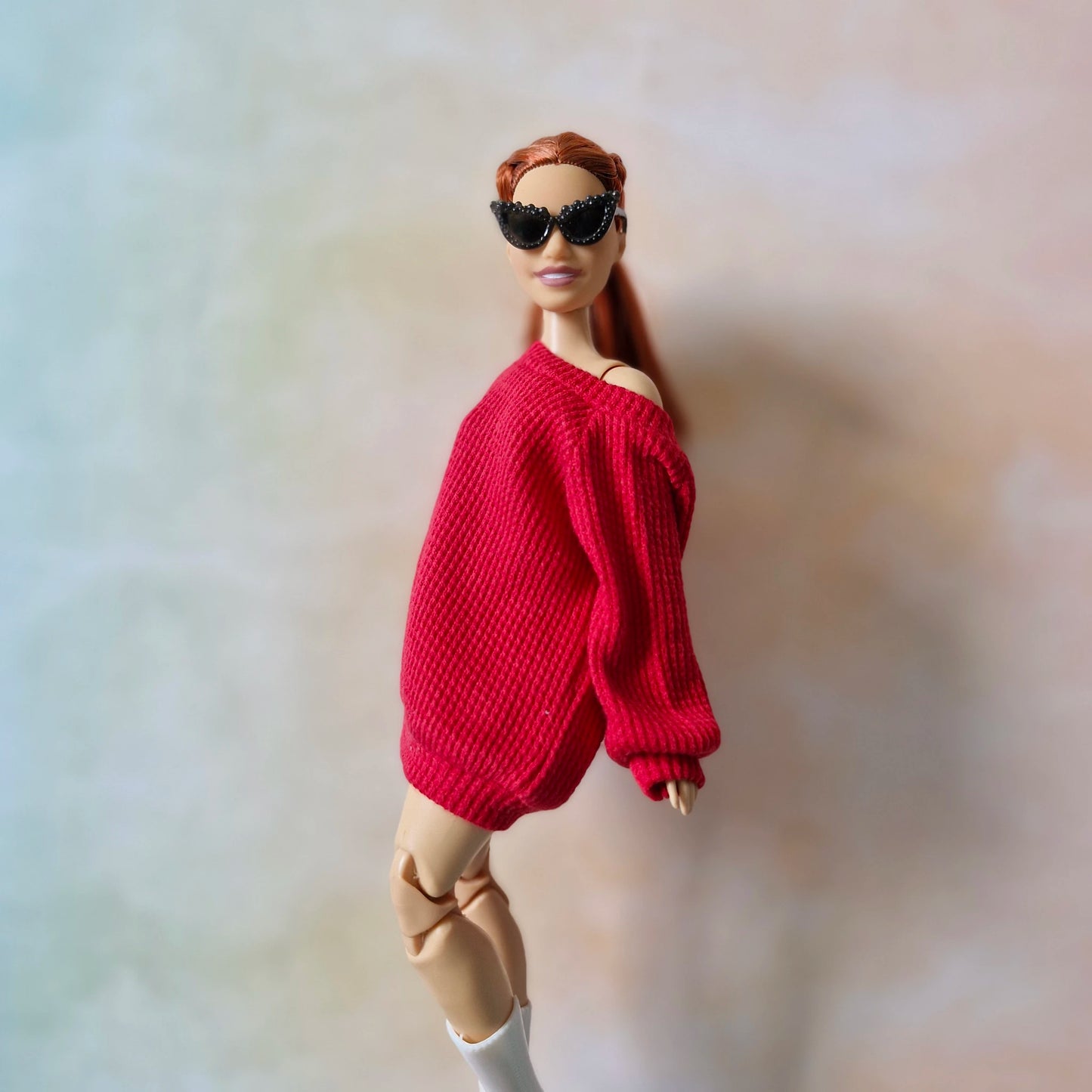 Barbie doll wearing a red sweater and sunglasses on a plain background