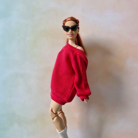 Barbie doll wearing a red sweater and sunglasses on a plain background