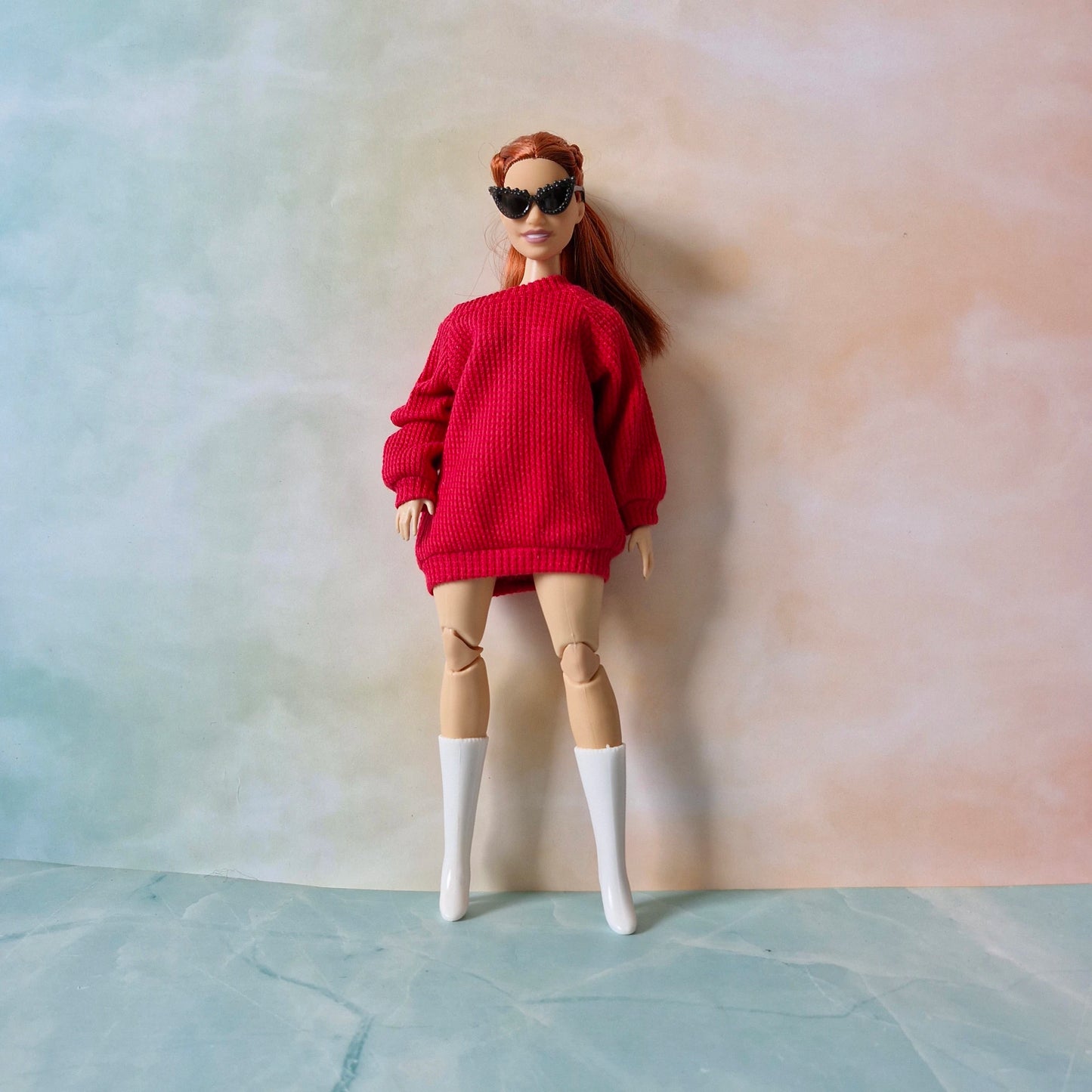 Doll wearing a red sweater, beige leggings, and white boots against a plain background