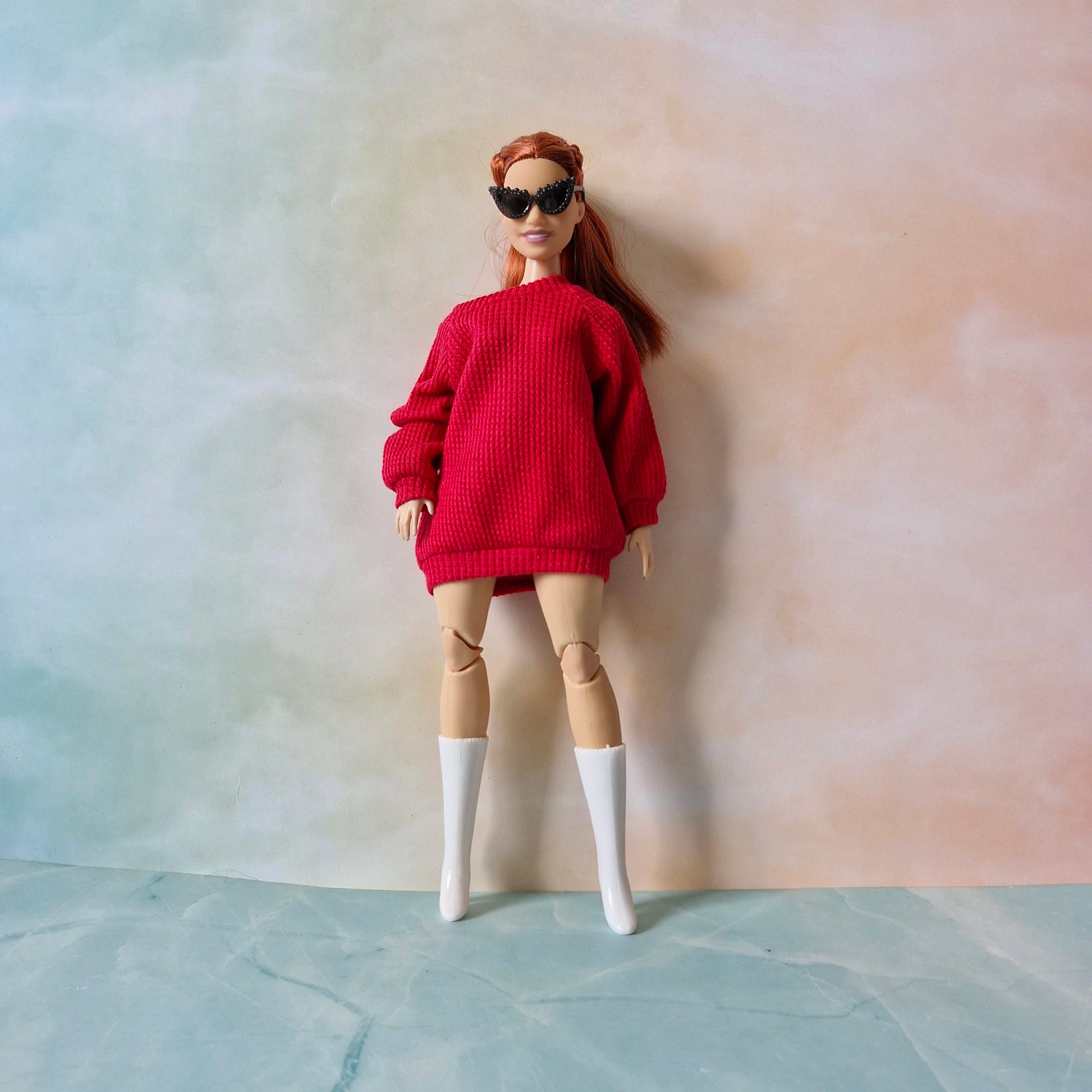 Doll wearing a red sweater, beige leggings, and white boots against a plain background
