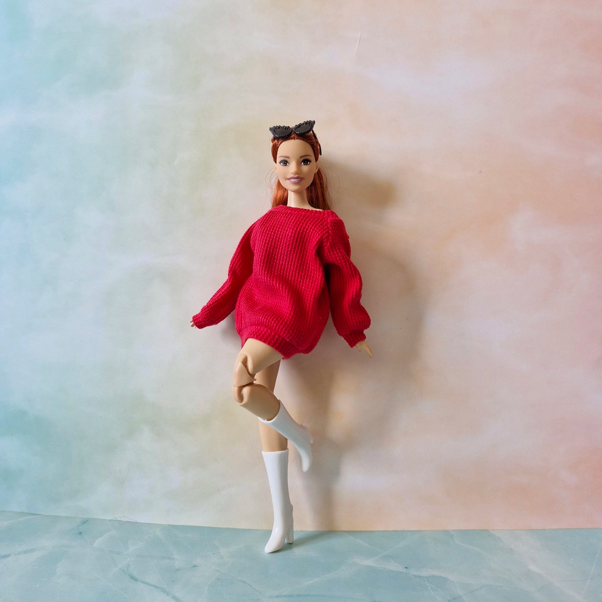 Barbie doll wearing a red sweater and white boots on a plain background