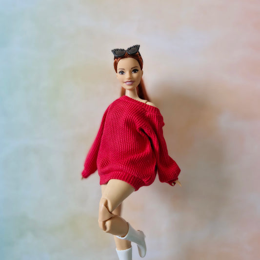 Barbie doll wearing a red sweater on a plain background