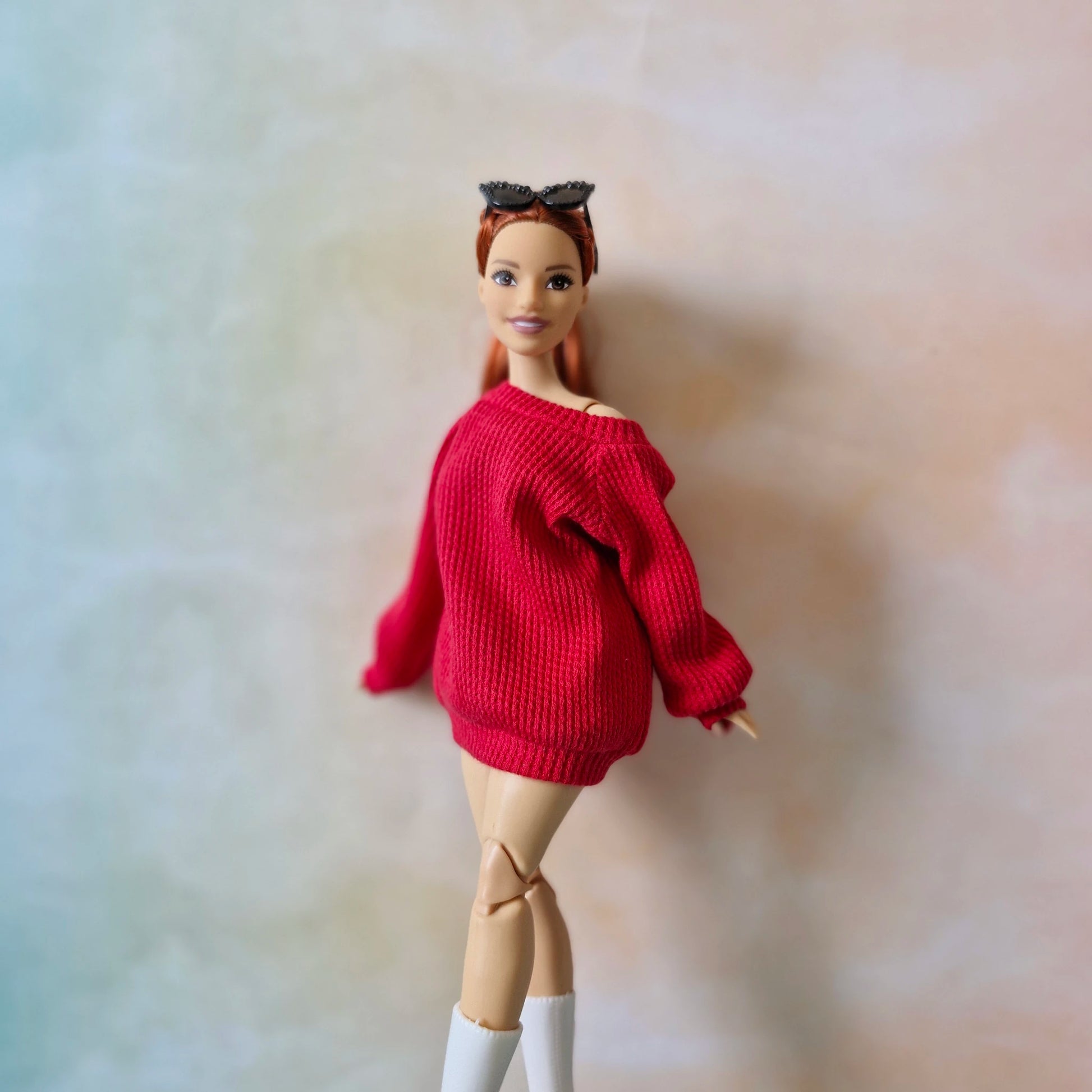 Barbie doll wearing a red sweater on a plain background