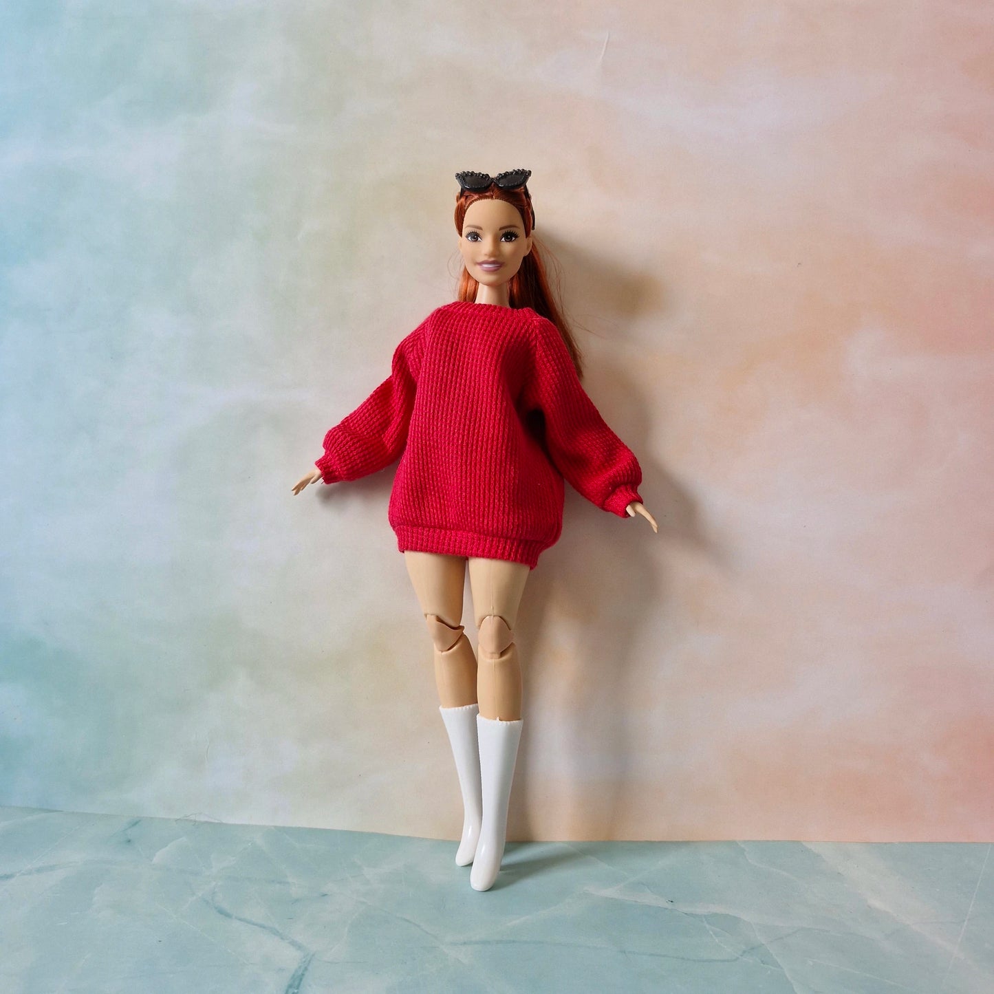Barbie doll wearing a red sweater and white boots against a gradient background