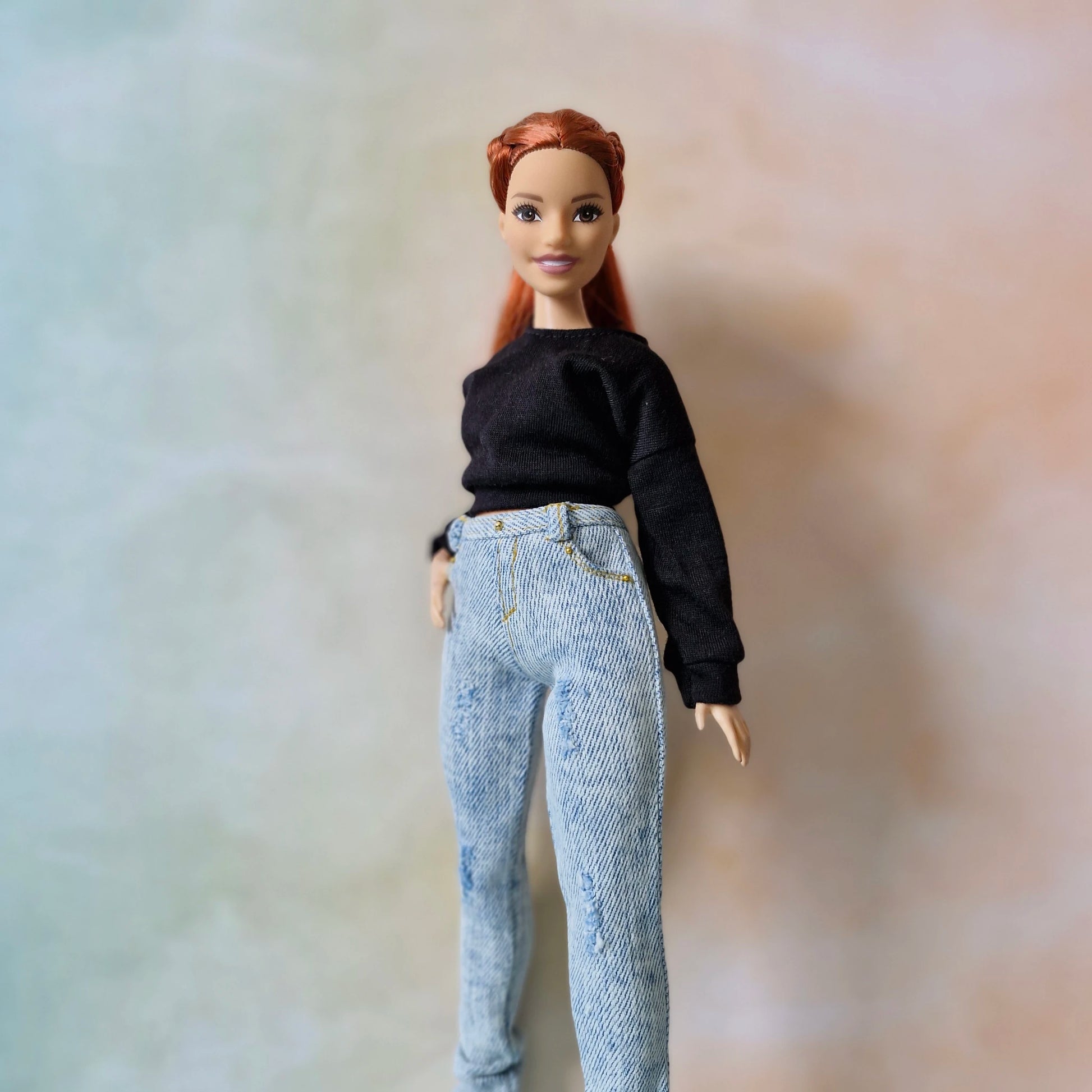 Barbie doll wearing a black top and blue jeans against a blurred background