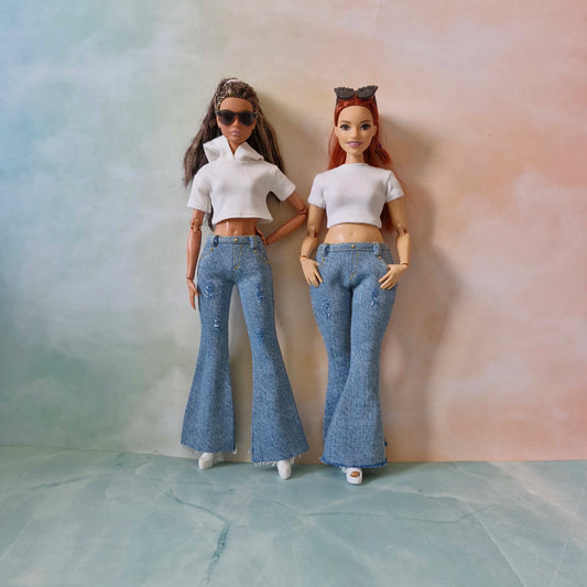 Two dolls wearing white tops and blue jeans against a gradient background