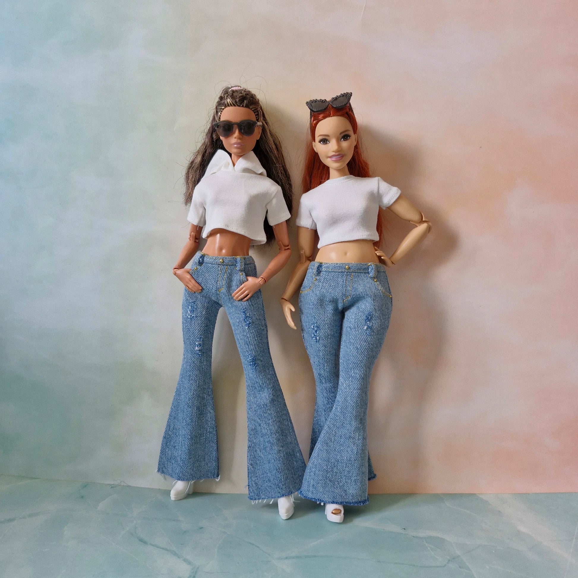 Two dolls wearing white tops and blue jeans against a gradient background