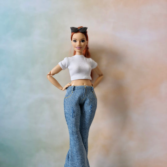 Barbie doll wearing a white top and blue jeans against a blurred background