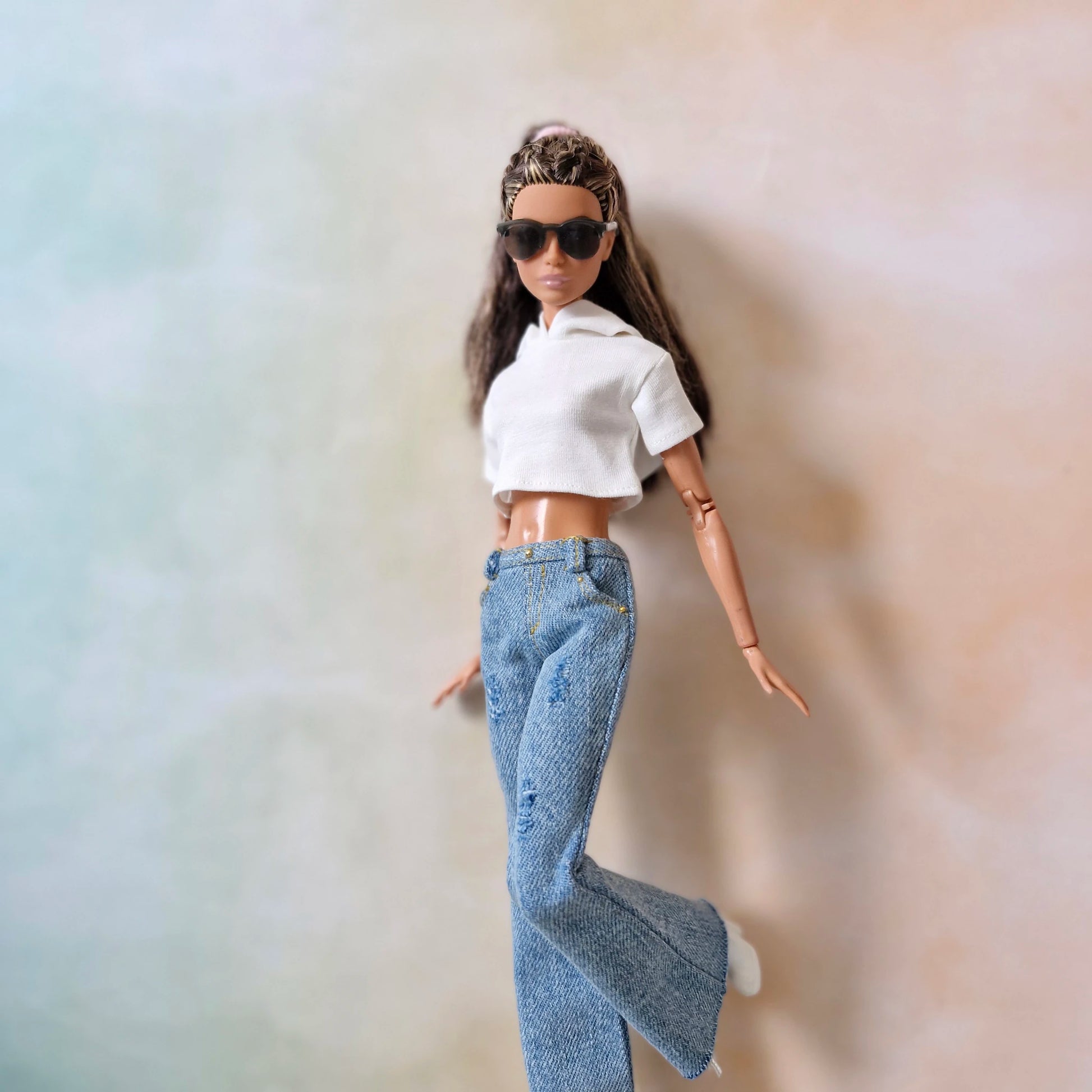 Barbie doll wearing sunglasses and a white top with blue jeans against a gradient background