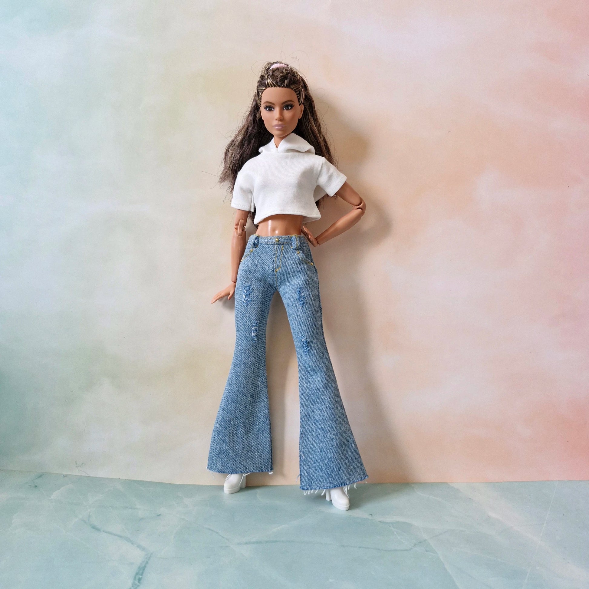Doll wearing a white crop top and blue flared jeans against a pastel gradient background