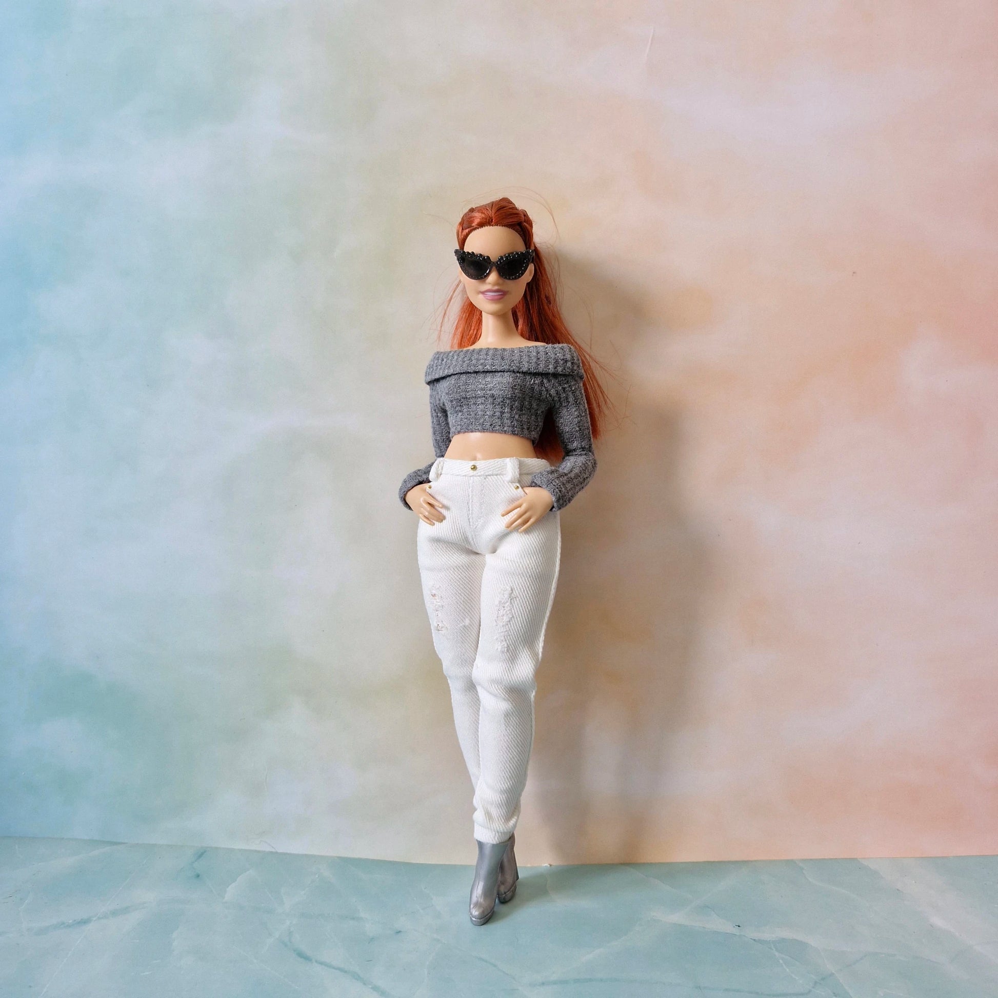 Barbie doll wearing a gray off-shoulder top and white pants against a gradient background